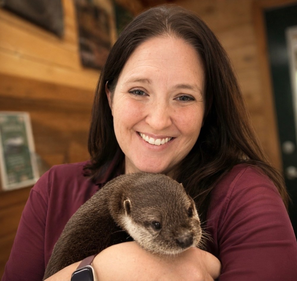 Smiling woman holding a small otter in a cozy indoor setting.