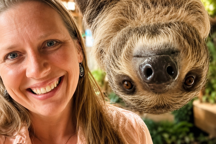 Woman smiling with a sloth hanging upside down beside her.