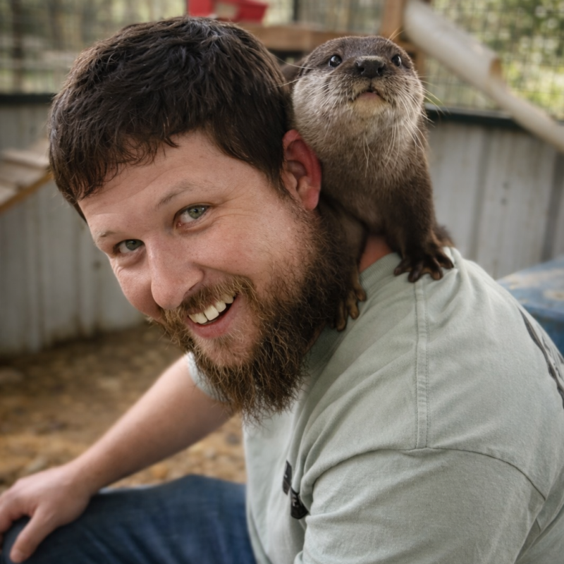 Smiling man with a small otter perched on his shoulder indoors.