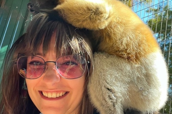 Woman with sunglasses smiling as a lemur sits on her shoulder.