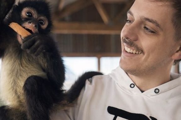 Person smiling at a monkey holding a carrot inside a building.